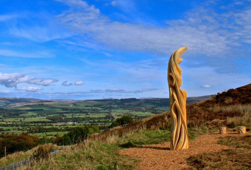 tall wooden sculpture on top of hill over looking view